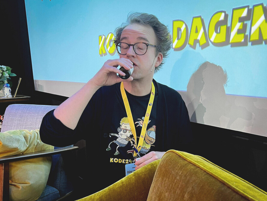 En forkjøla kode24-redaktør Ole Petter Baugerød Stokke hiver i seg hostesaft for å klare å gjennomføre kode24-dagen tidligere i år, med hundrevis av leserne i salen - ikke på Facebook. 📸: Jørgen Jacobsen