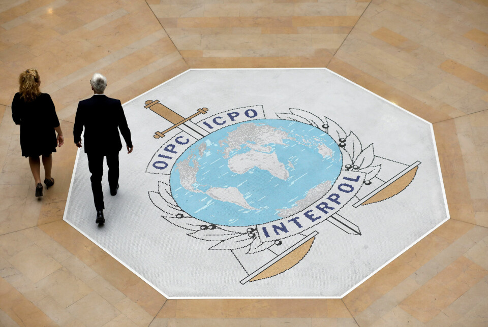 Interpol har fått seg en norsk global sikkerhetssjef. Bjørn Richard Watne tok over som CISO 1. juli i år. Bildet er av to personer, en mann og en kvinne, i svarte penklær, som går gjennom et stort, åpent rom inne i Interpols lokaler. Bildet er tatt ovenfra. På gulvet er Interpollogoen, en jordklode foran et vertikalt sverd og over to vektskåler.