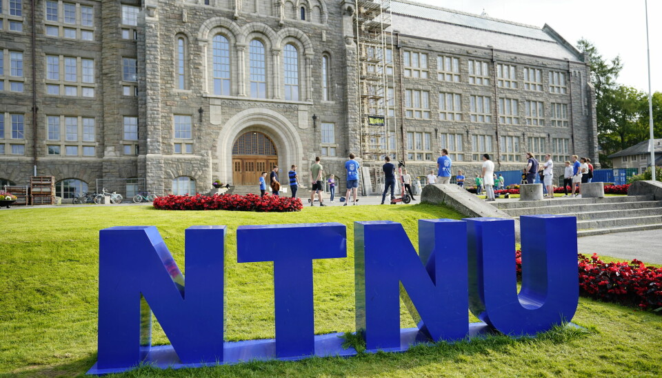 NTNU er også ramma av dataangrepet som ble omtalt i starten av uka. Bildet er av NTNU-logoen på en grønn gressplen foran et gammelt universitetsbygg. Det er folk som går foran bygget.