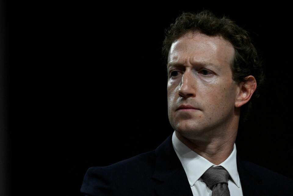 Mark Zuckerberg, her under en høring i det amerikanske senatet, slipper å vitne i et søksmål om Cambridge Analytica-skandalen. Det ble klart etter at han med flere inngikk et forlik. Bildet er av en mann i mørk dress mot mørkbakgrunn. Han har hvit skjorte og grått slips. Mannen har en alvorlig mine. Det er Mark Zuckerberg.